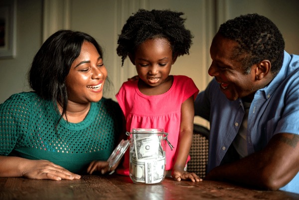 A family smiling around a jar of savings
